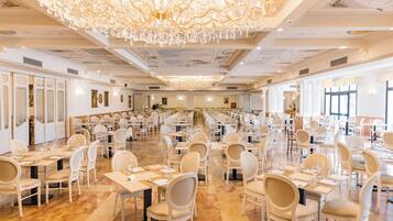 A large banquet hall with numerous tables and chairs, a grand chandelier, and a high ceiling with intricate designs.