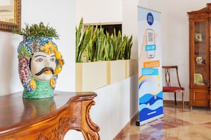 A reception area with a decorative vase, a wooden reception desk, a plant display, and a digital information kiosk. - Delfino Beach Hotel (Marsala)