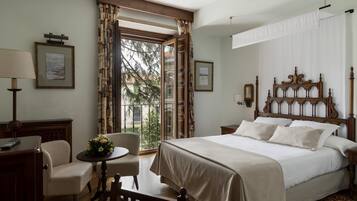 A hotel room with a large bed, a desk with a lamp, a chair, and a view of the outdoors through a window.