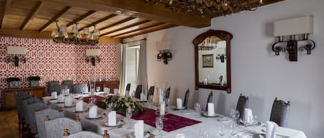 Un comedor con una larga mesa dispuesta para una comida, vigas de madera en el techo y papel tapiz estampado.