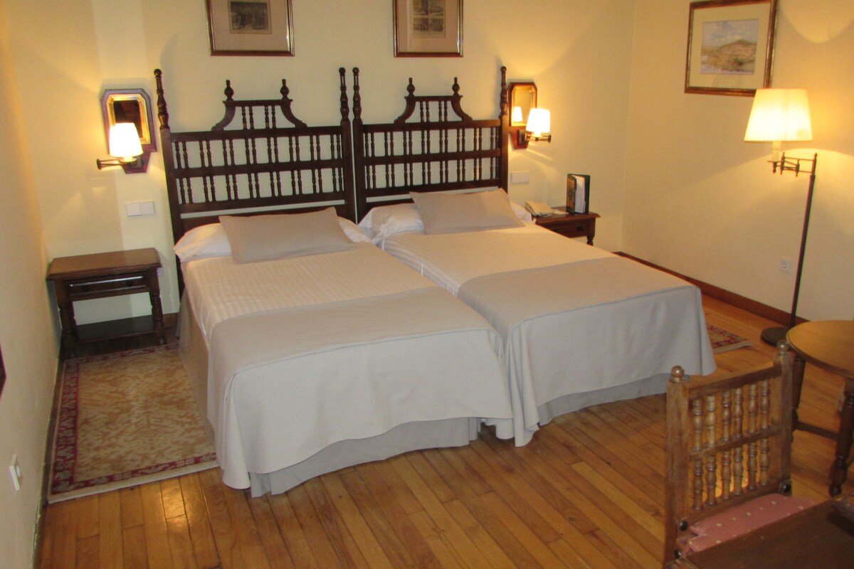 Una cama doble con cabecera de madera, dos mesitas de noche, una silla y una lámpara de pie.