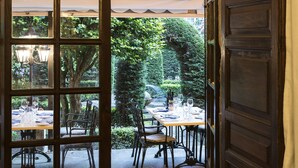 An open door leading to an outdoor dining area with tables and chairs, surrounded by greenery.