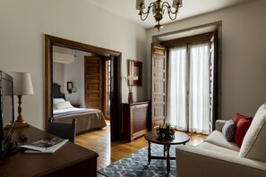 A hotel room with a bed, a sitting area with a sofa and a coffee table, a desk with a lamp, and a large mirror.