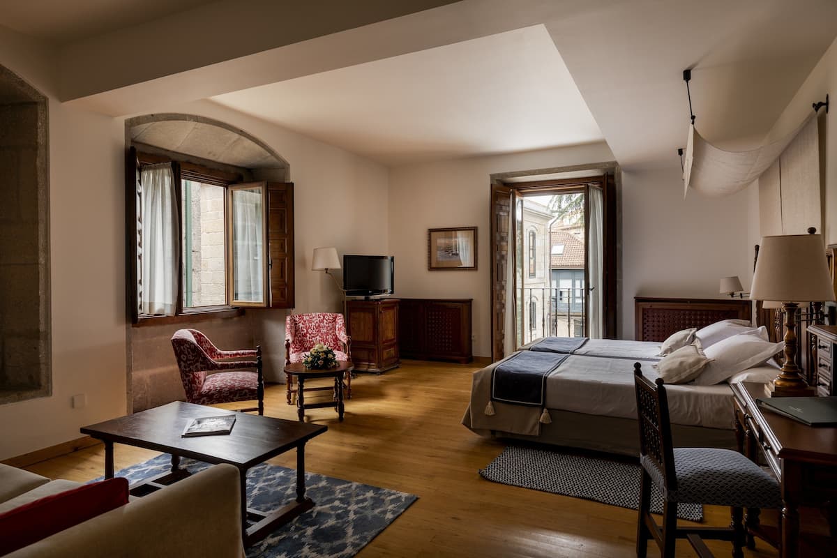 A hotel room with a bed, a desk, a chair, a television, and a window with curtains.