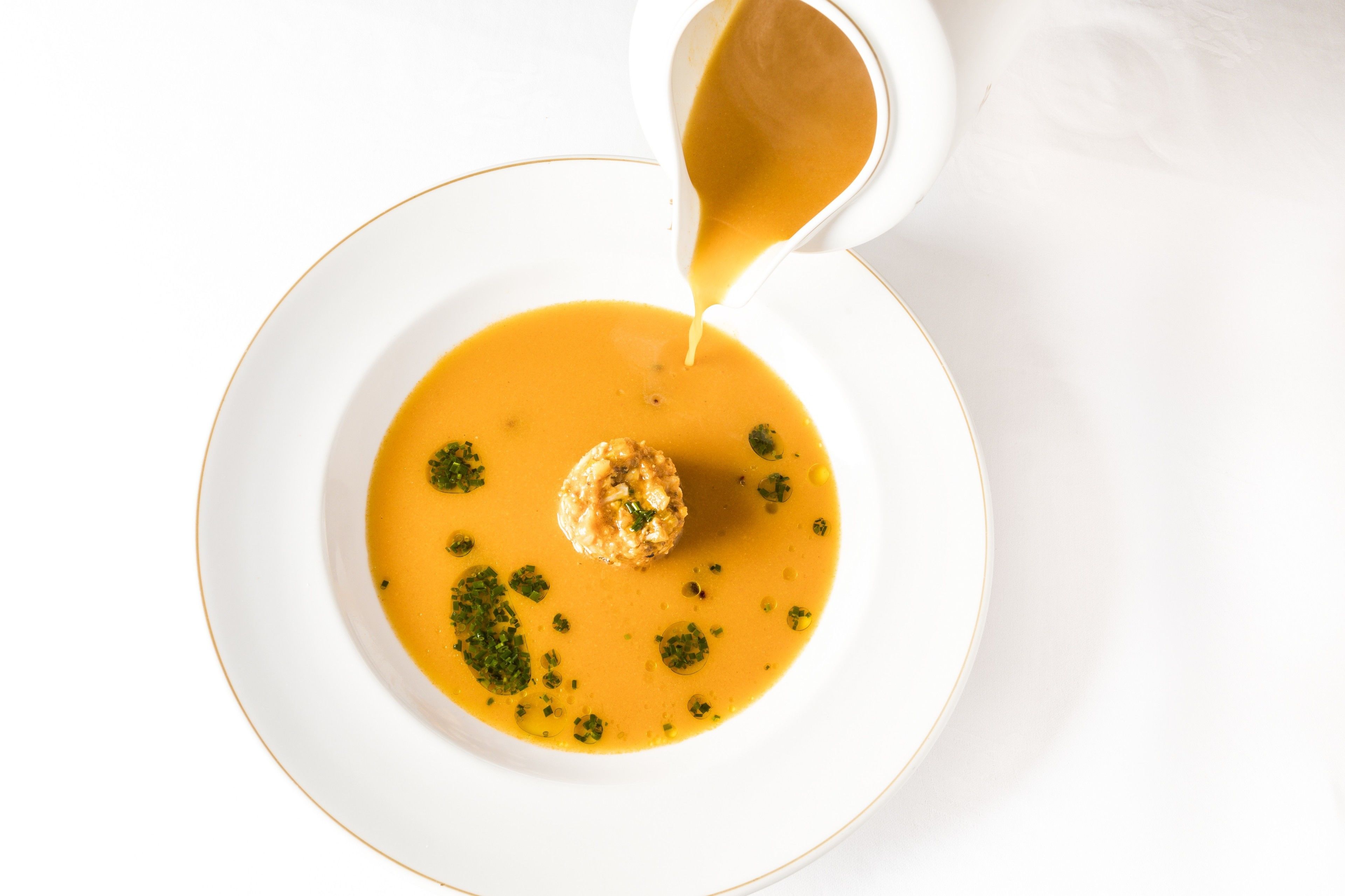 A white plate with a soup and a dumpling, garnished with herbs.