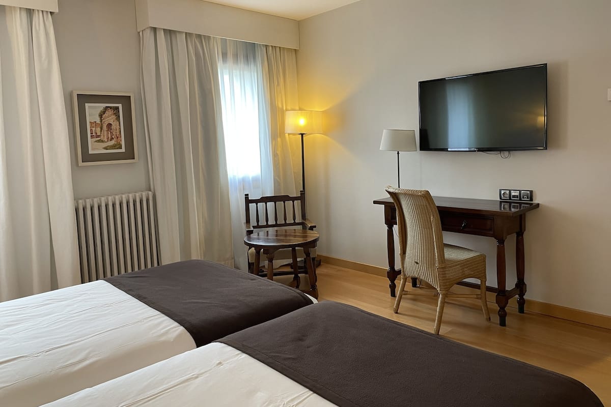 Une chambre d’hôtel avec deux lits, un bureau avec une chaise, une télévision et une lampe.