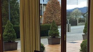 A room with a round table and chairs, a window with curtains, and a view of a courtyard with potted plants and a sign that reads "TIRAR". - Parador de Puebla de Sanabria (Puebla de Sanabria)