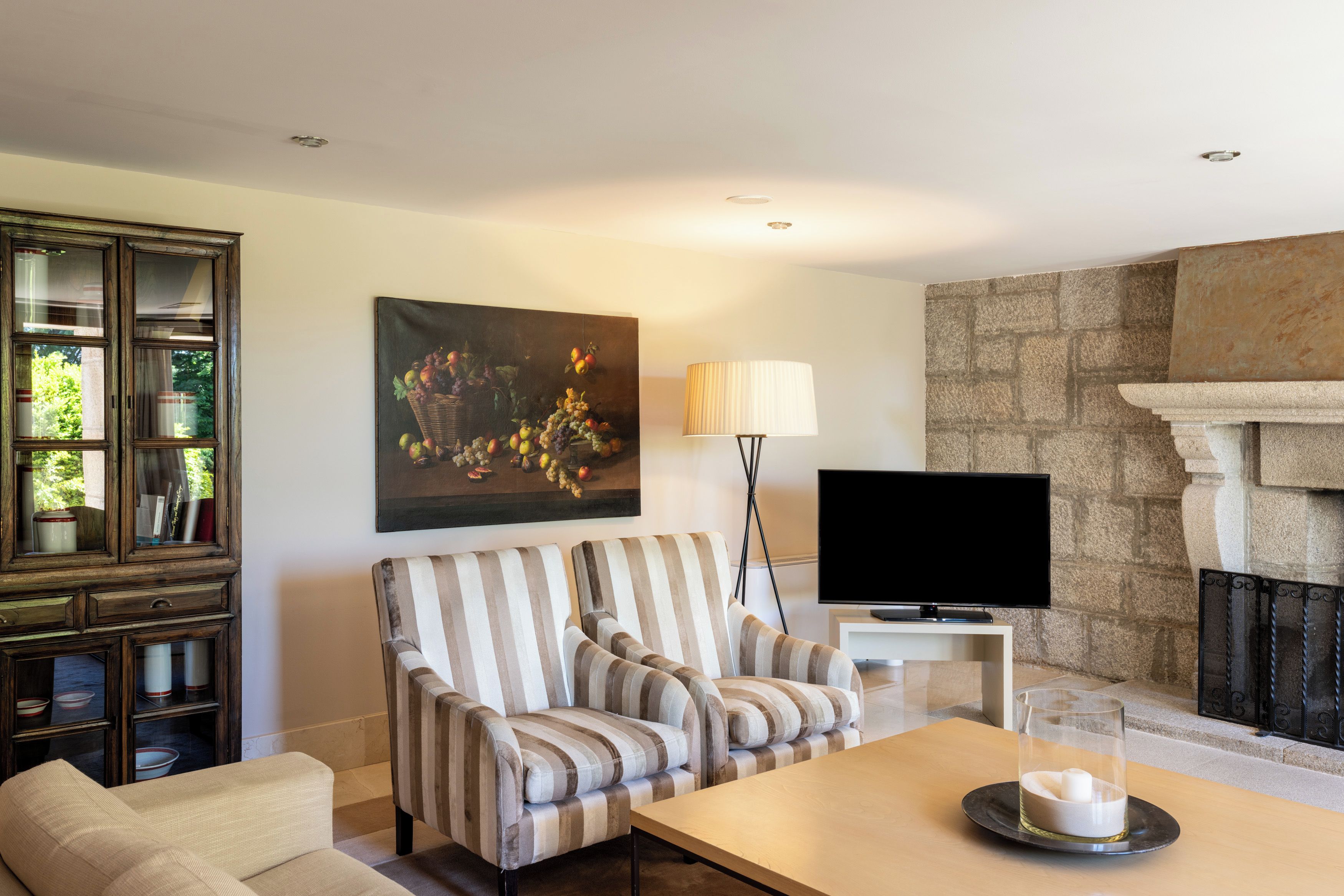 Una sala de estar con chimenea, televisor, un sofá a rayas y un cuadro con frutas.