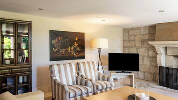 Una sala de estar con chimenea, televisor, un sofá a rayas y un cuadro con frutas.