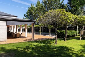Un patio techado con mobiliario exterior, rodeado de un césped cuidado y árboles.