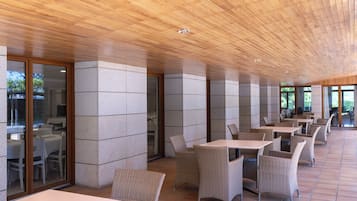A covered outdoor seating area with tables and wicker chairs, stone pillars, and a wooden ceiling.
