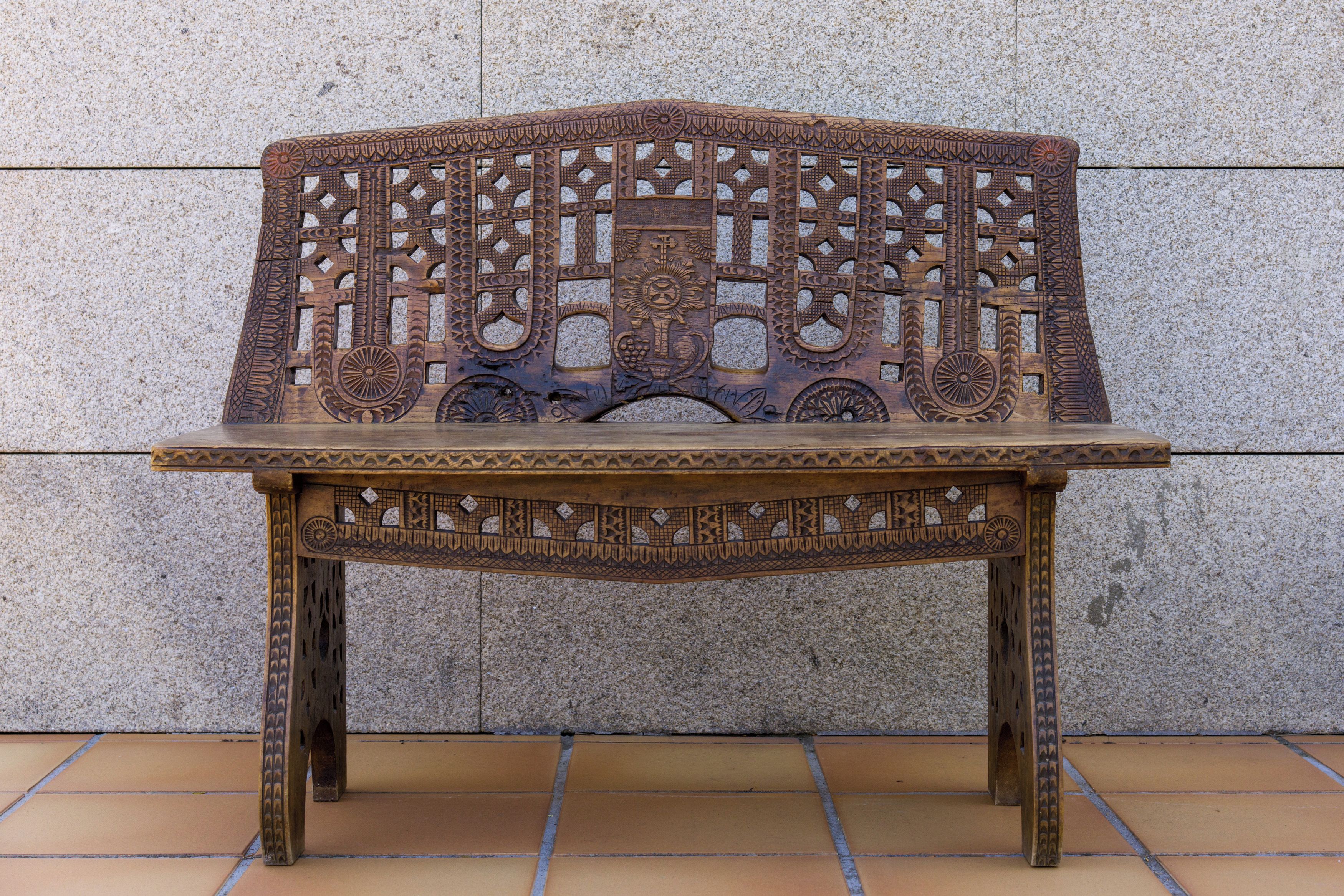 A wooden bench with intricate carvings against a stone wall.