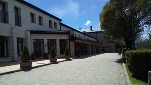 A paved courtyard with potted trees, a building with multiple windows and a covered entrance, and a street lamp. - Parador de Puebla de Sanabria (Puebla de Sanabria)