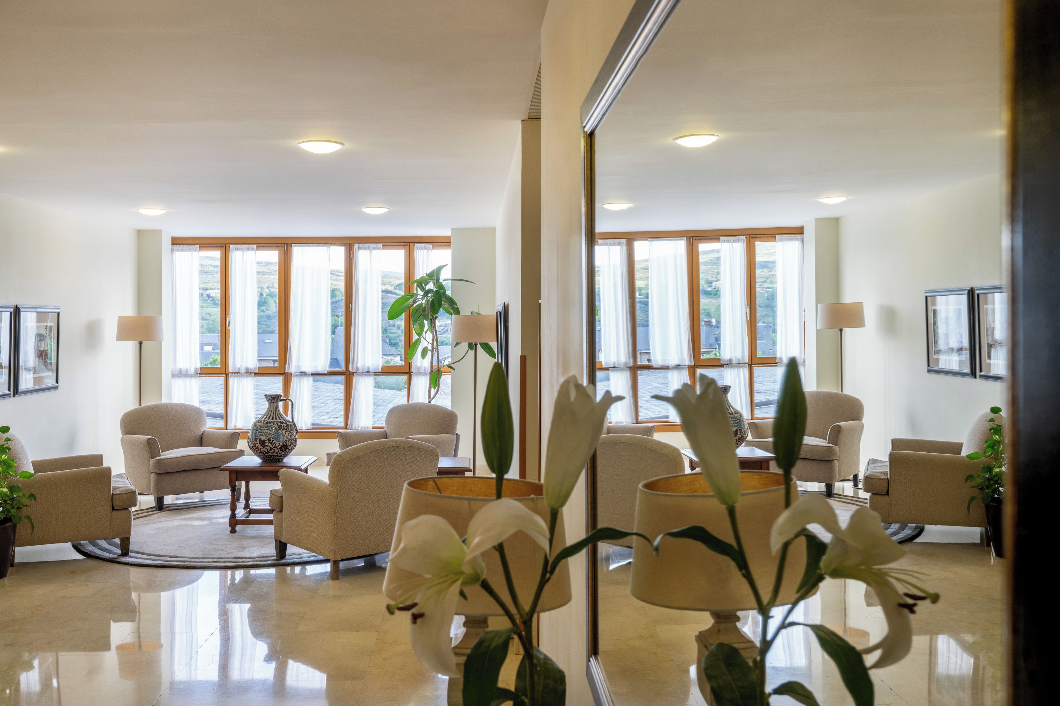 Un vestíbulo de hotel con diseño moderno, que cuenta con una zona de estar con sofás y sillones, una mesa de centro y un jarrón grande con una planta.