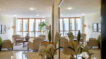 Un vestíbulo de hotel con diseño moderno, que cuenta con una zona de estar con sofás y sillones, una mesa de centro y un jarrón grande con una planta.