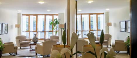 Un vestíbulo de hotel con diseño moderno, que cuenta con una zona de estar con sofás y sillones, una mesa de centro y un jarrón grande con una planta.