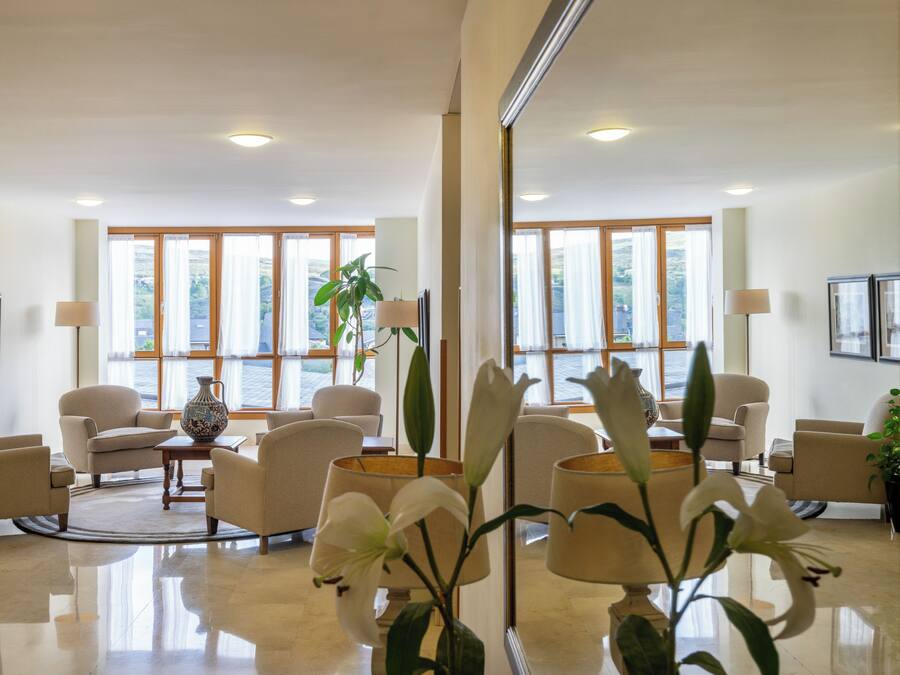 A hotel lobby with a modern design, featuring a seating area with sofas and armchairs, a coffee table, and a large vase with a plant.