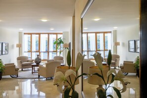 Un vestíbulo de hotel con diseño moderno, que cuenta con una zona de estar con sofás y sillones, una mesa de centro y un jarrón grande con una planta.