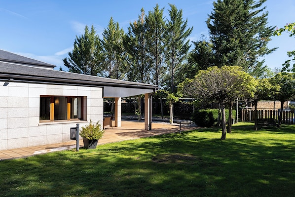 A modern house with a covered patio, a lawn, and tall trees in the background.