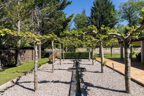 A garden with a gravel pathway, trees, and a wooden pergola.