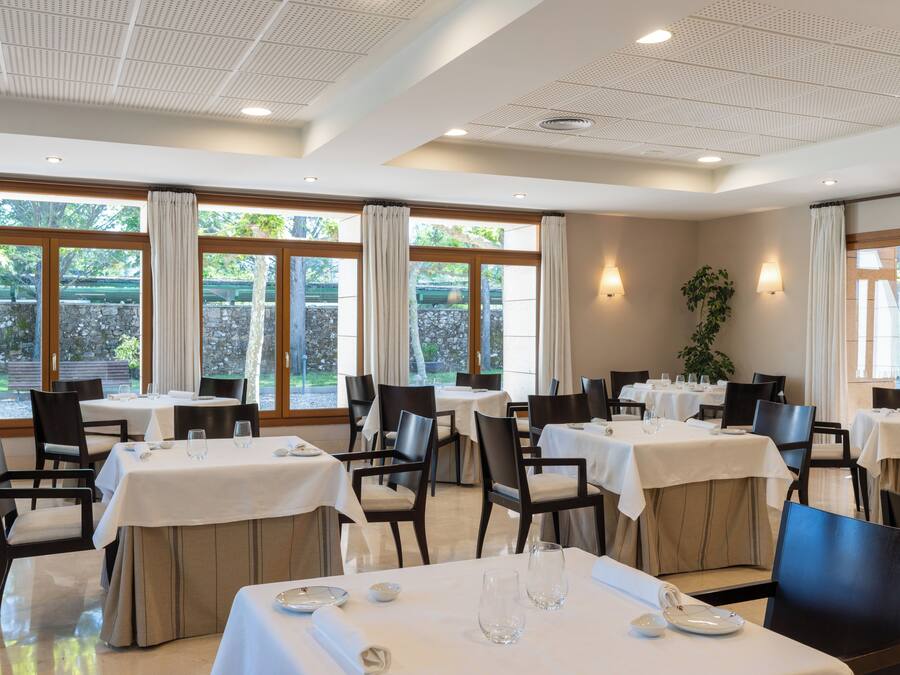 A restaurant with multiple tables, chairs, and large windows with curtains.