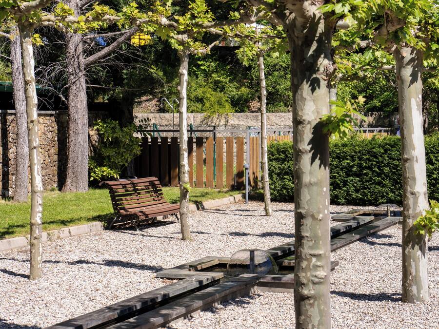 A park with a gravel path, a wooden bench, and a metal fence.