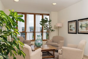 Sala de estar con una mesa de centro de madera, sofás beige, un ventanal con cortinas, una planta en maceta y cuadros en la pared.