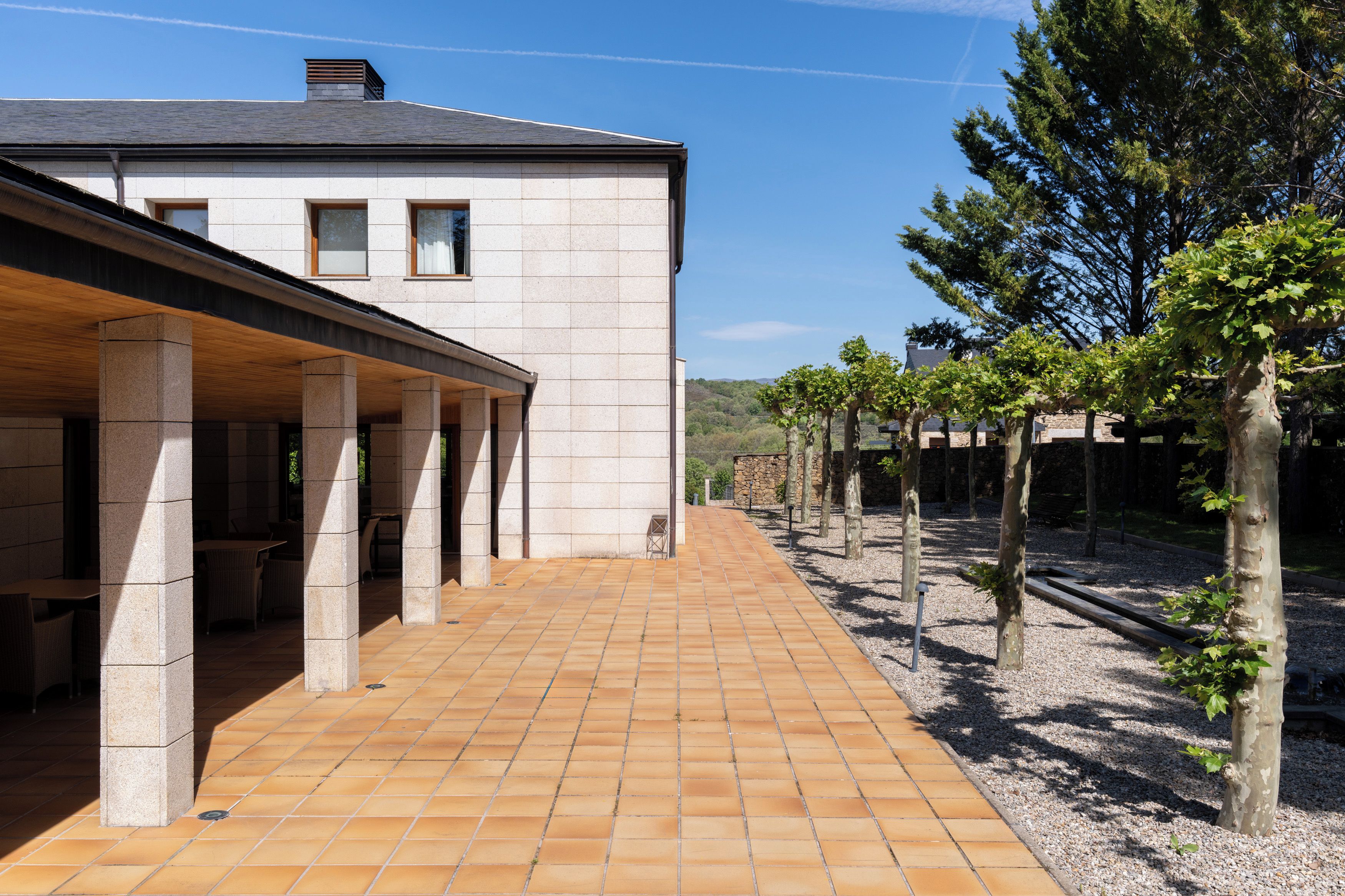 Un edificio con un patio cubierto, columnas de piedra y un camino empedrado.