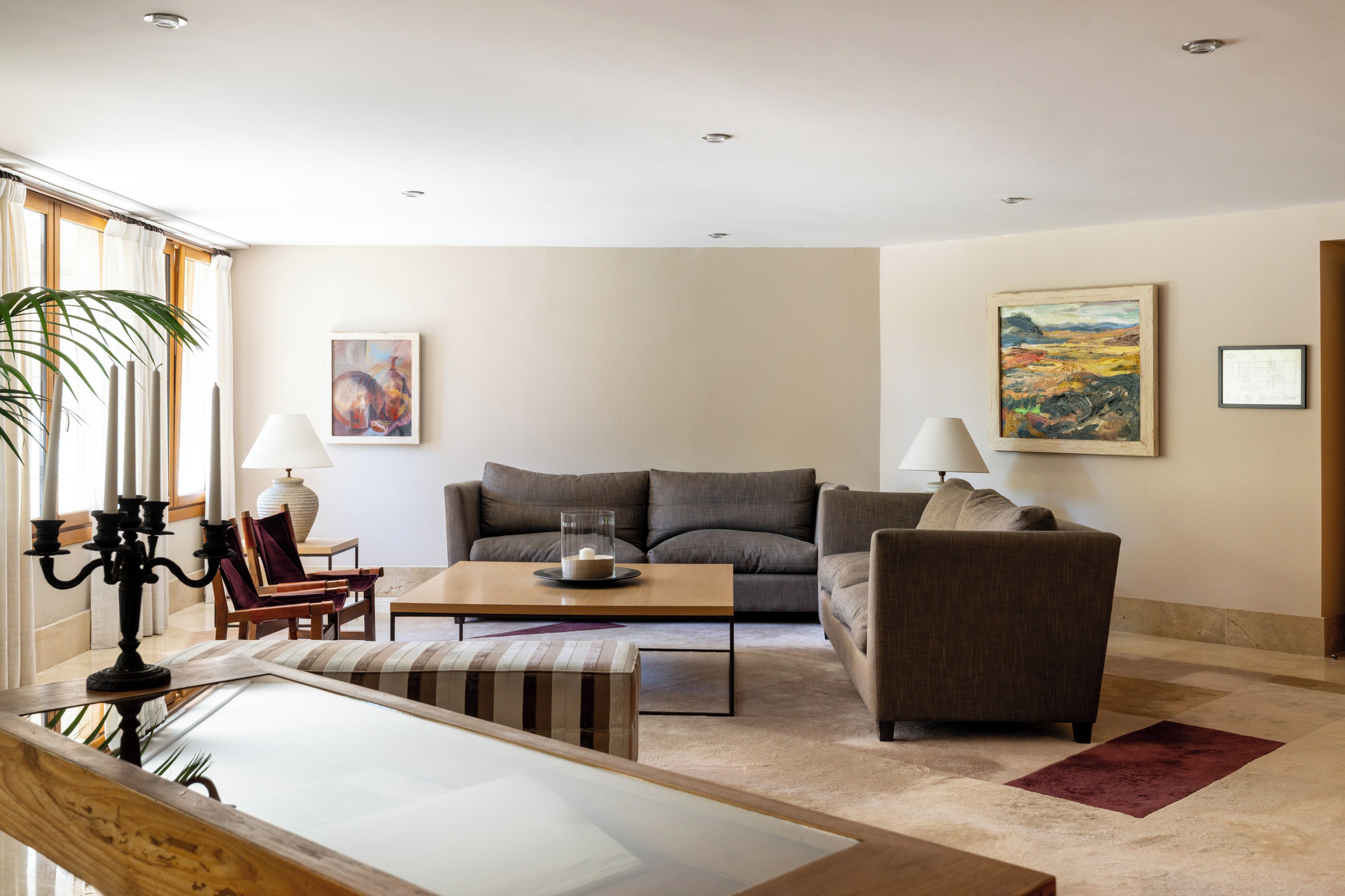 Un salon moderne comprenant un canapé, des fauteuils, une table basse et une table à manger. On y trouve deux lampes, un tableau et une reproduction encadrée d’un plan architectural accrochés aux murs.