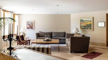 Una sala moderna con un sofá, sillones, una mesa de centro y una mesa de comedor. Hay dos lámparas, un cuadro y un plano arquitectónico enmarcados en las paredes.