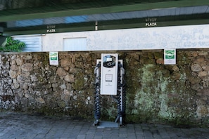 Un área de estacionamiento con estaciones de carga para vehículos eléctricos, un muro de piedra y un edificio con un cartel que dice 'PLAZA'.