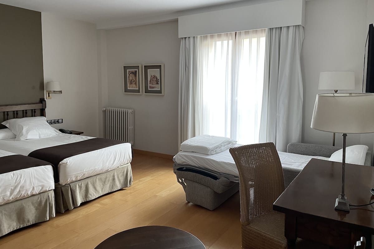 Une chambre d’hôtel avec deux lits, un bureau, une chaise, un radiateur et deux tableaux encadrés au mur.