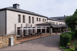 A building with a stone facade, outdoor seating area with umbrellas, and a paved entrance.