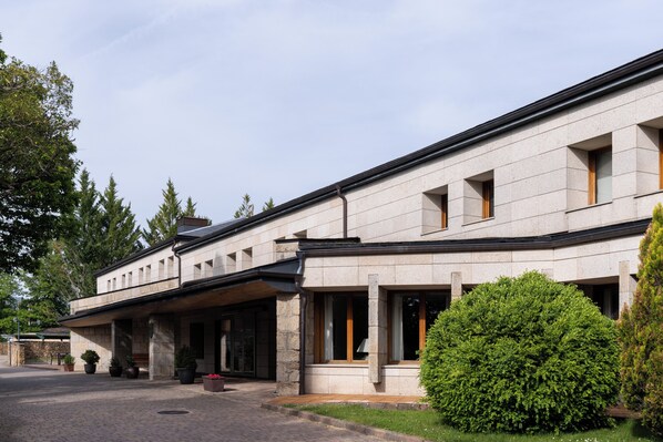 Un edificio moderno con fachada de piedra, ventanas amplias y un área de entrada cubierta con plantas en macetas.