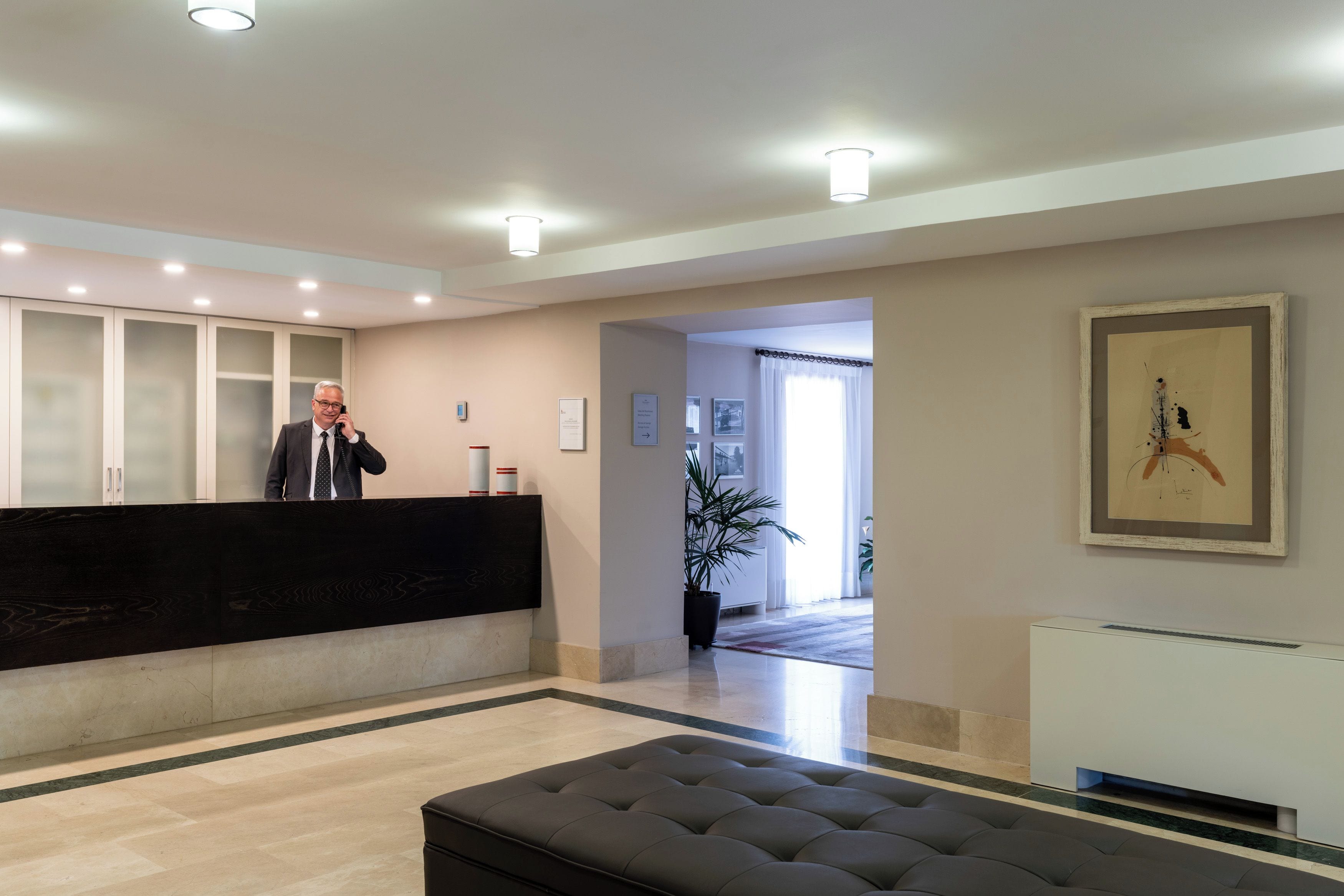 Zona de recepción de un hotel, con mostrador de recepción, área de espera con un banco y una obra de arte enmarcada en la pared.