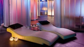Un moderno spa con dos sillones reclinables, una mesita con una bebida y luces decorativas.