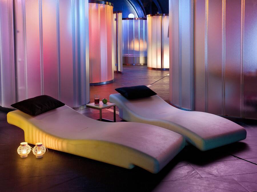 Un moderno spa con dos sillones reclinables, una mesita con una bebida y luces decorativas.