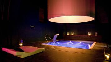Una piscina interior climatizada con un sillón de masaje, una lámpara colgante grande y velas a un lado.