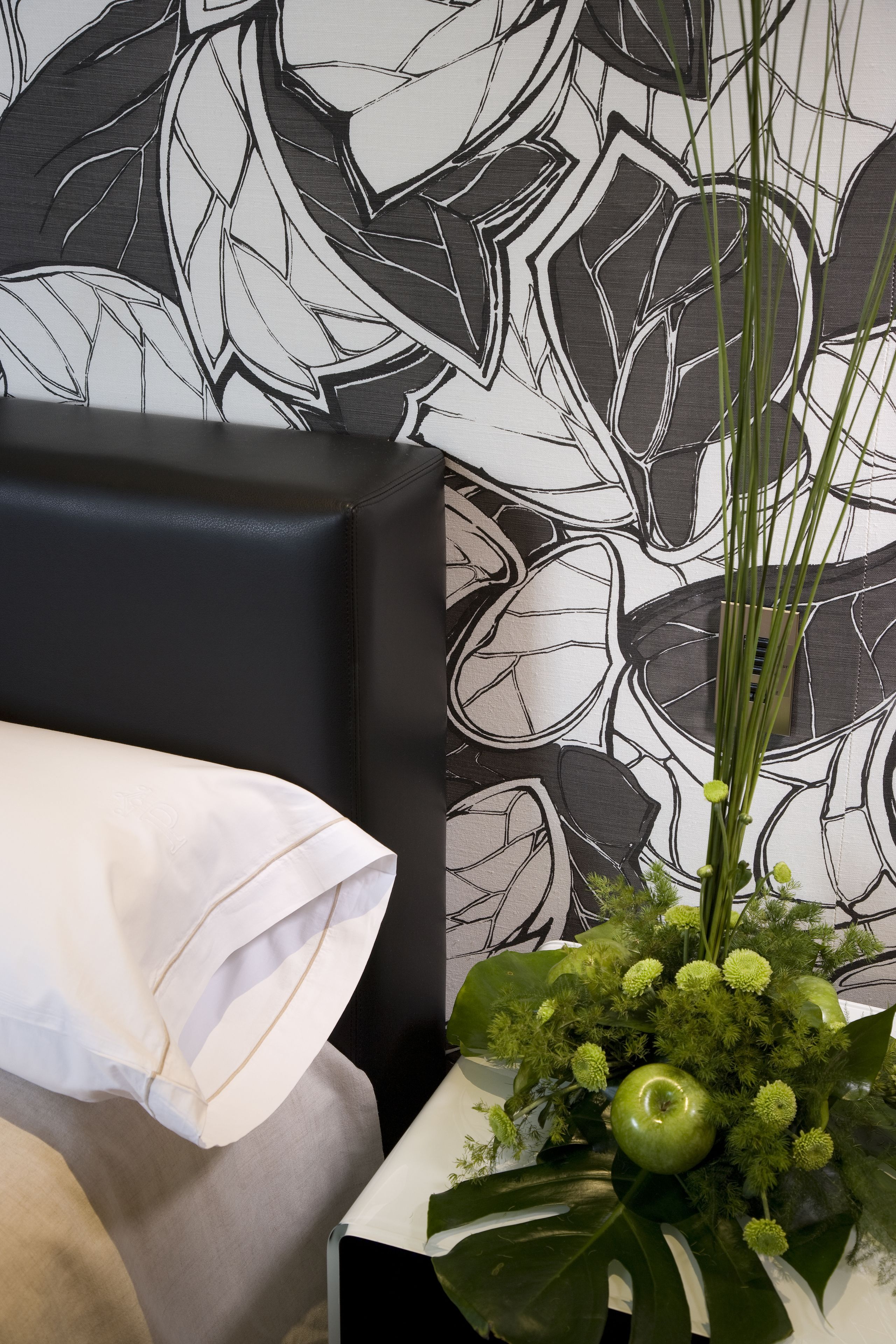 Une pièce avec un fauteuil en cuir noir, un coussin blanc et une table blanche sur laquelle se trouvent une pomme verte et quelques feuilles.