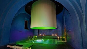 Um quarto de spa com um lustre cilíndrico grande, uma mesa de massagem e uma pequena piscina.