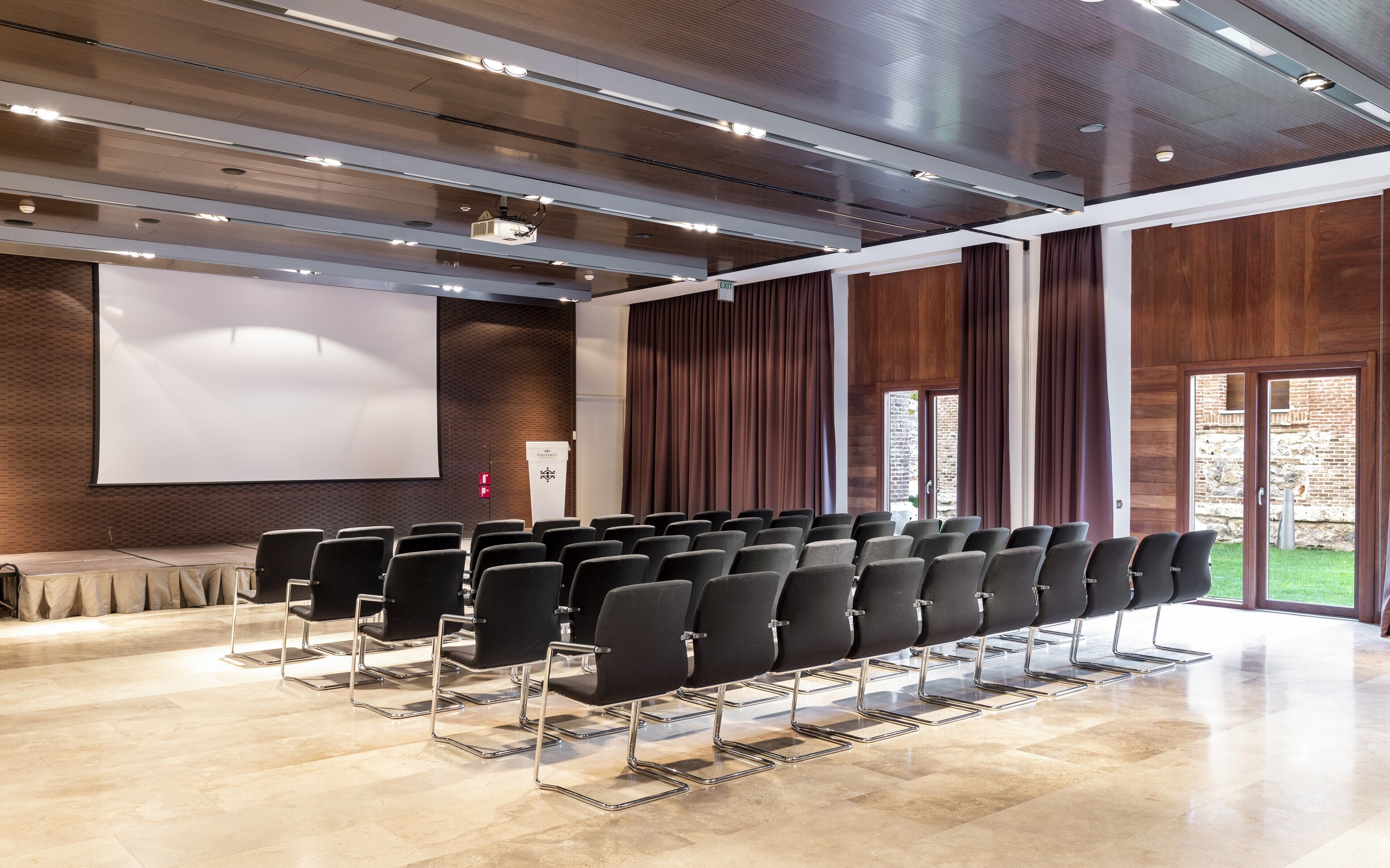 A modern conference room with rows of black chairs, a large screen, and wooden paneling.