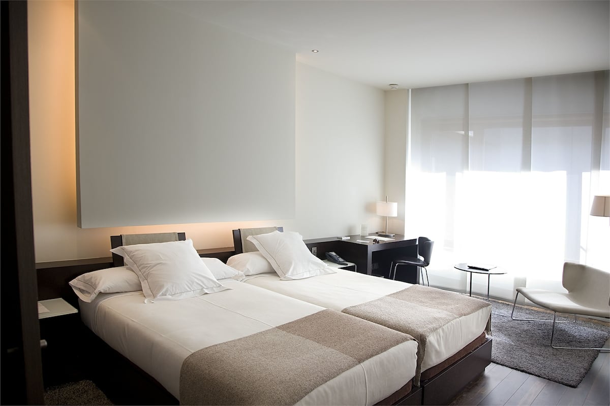 Une chambre d’hôtel avec deux lits, un bureau, une chaise et une grande fenêtre.