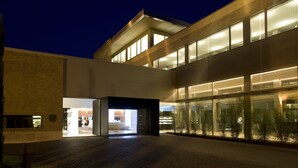 A modern building with a glass facade, a brick entrance, and a well-lit interior. - Parador De Alcala (Alcala de Henares)