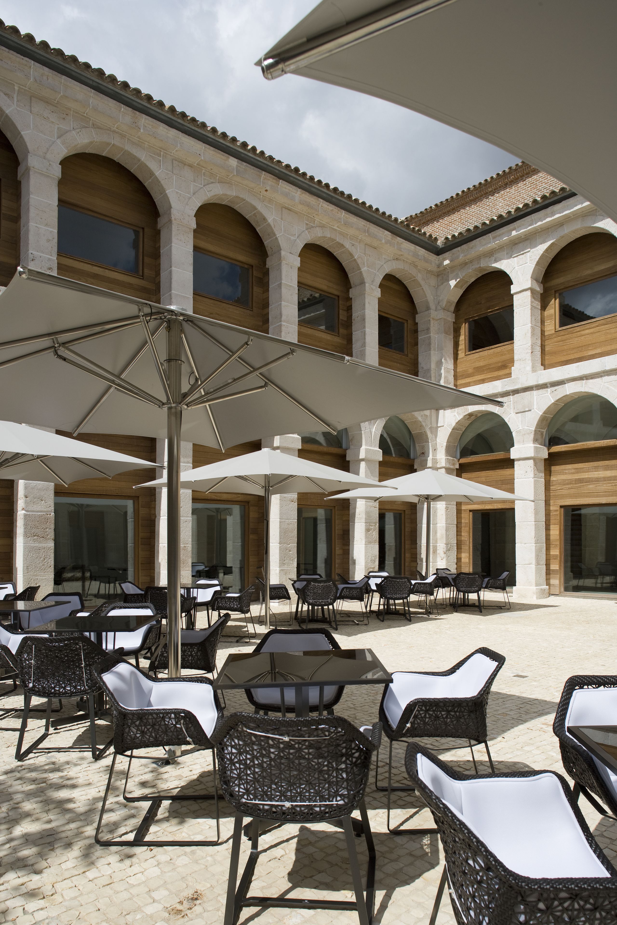 Un patio al aire libre con columnas de piedra, sombrillas blancas y sillas de mimbre.