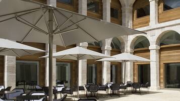 Un patio al aire libre con columnas de piedra, sombrillas blancas y sillas de mimbre.