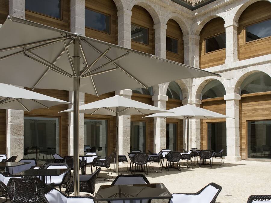 Un patio al aire libre con columnas de piedra, sombrillas blancas y sillas de mimbre.