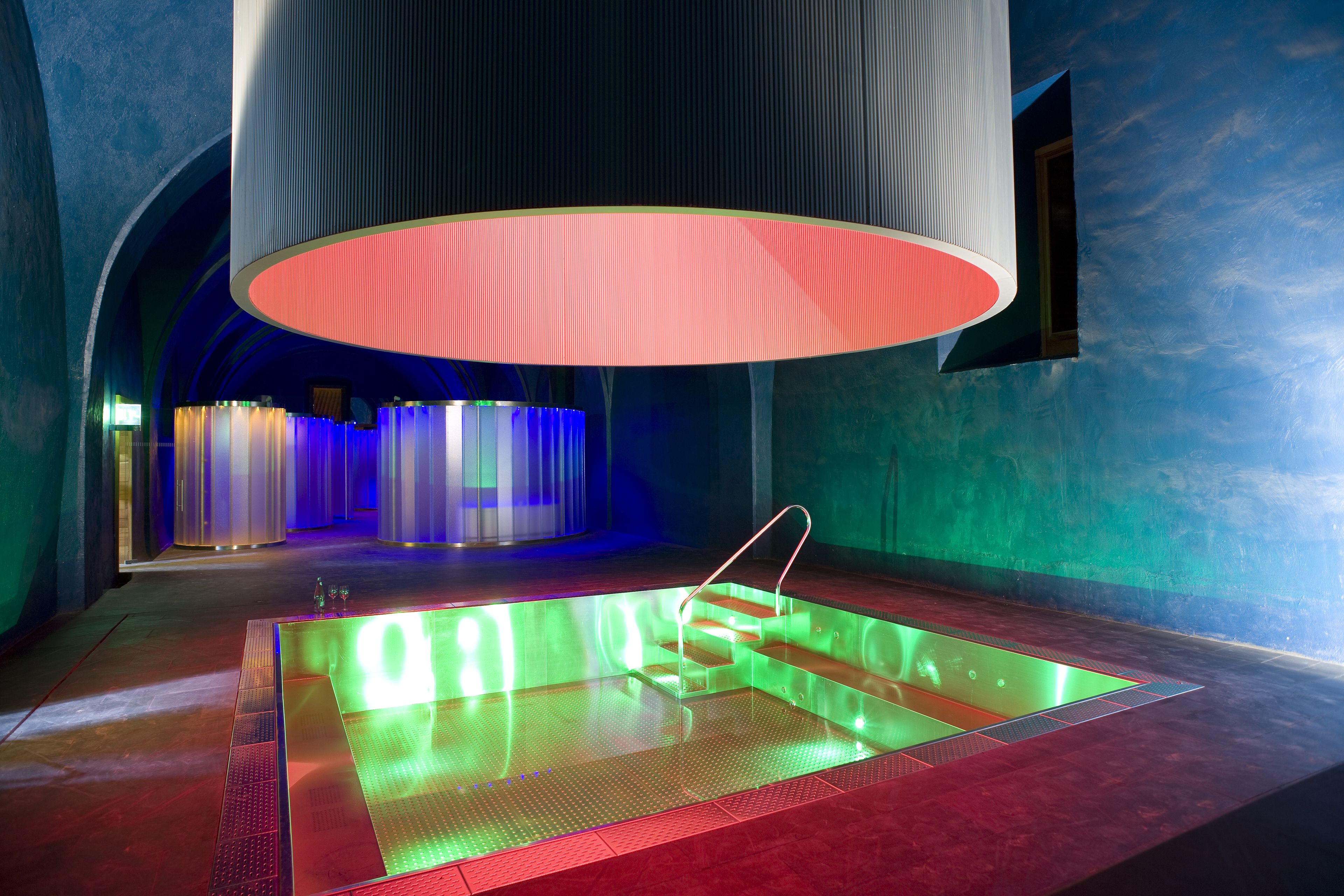 Una piscina interior moderna con un diseño de iluminación único, rodeada de paredes azules y una gran estructura iluminada en el techo.