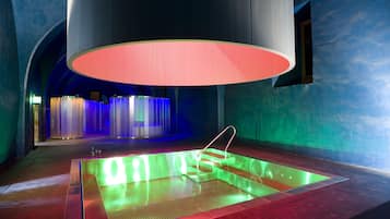 Une piscine intérieure moderne dotée d’un système d’éclairage original, entourée de murs bleus et surmontée d’une grande structure de plafond illuminée.