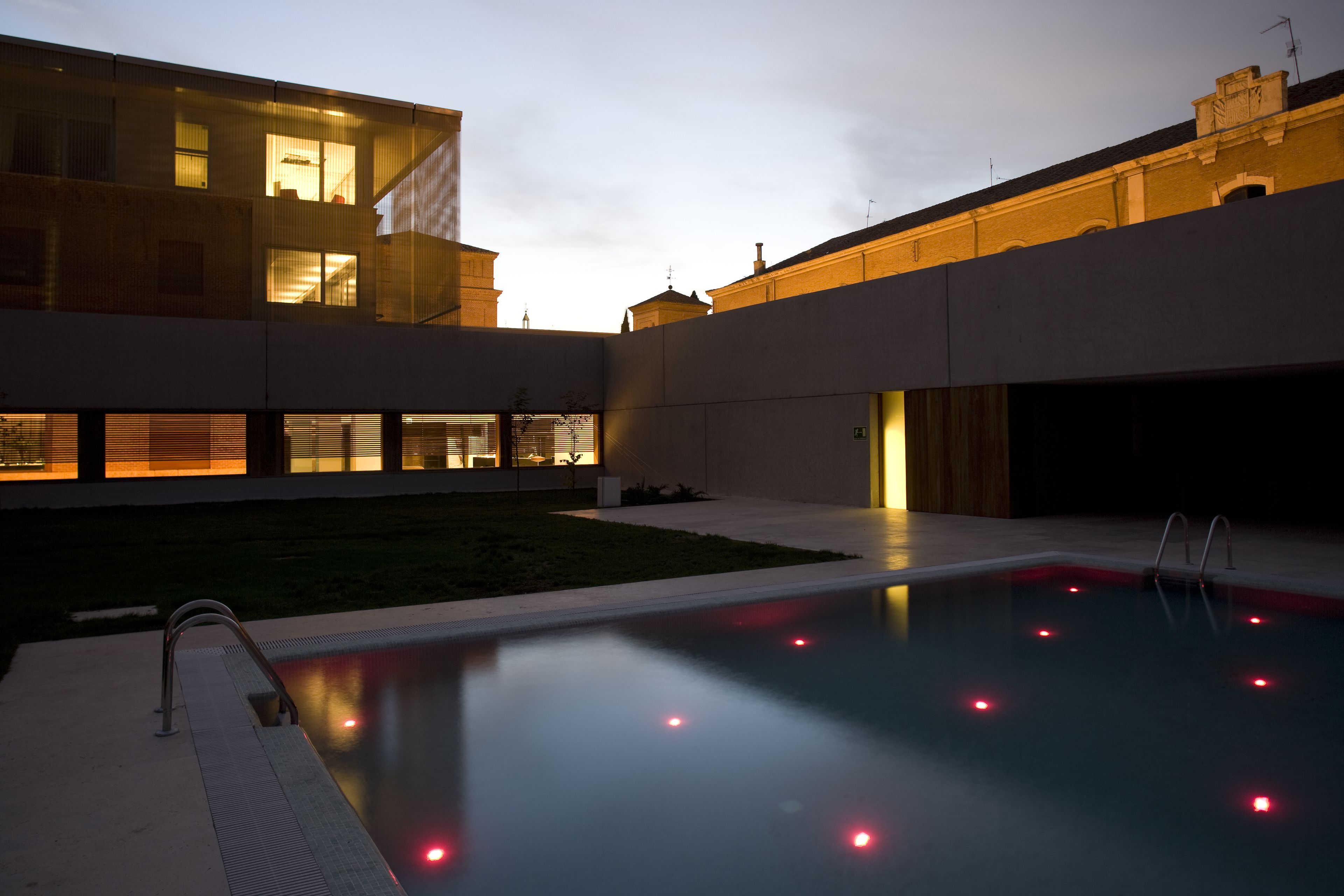 Un edificio moderno con piscina, ventanas amplias e iluminación exterior cálida al anochecer.
