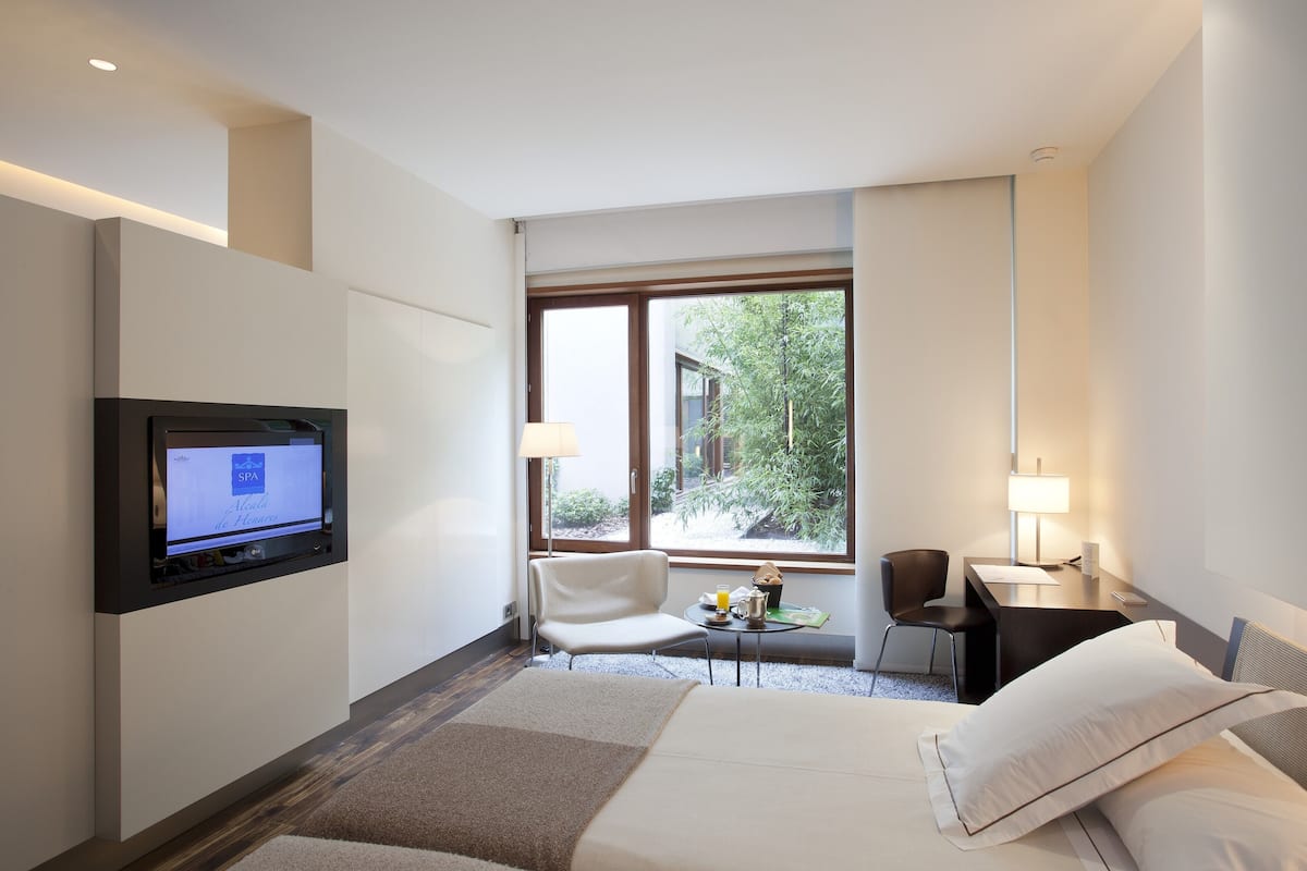 Une chambre d’hôtel équipée d’un lit, d’un bureau, d’une chaise, d’une télévision et d’une fenêtre donnant sur un paysage verdoyant.